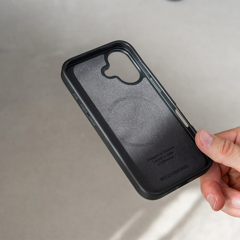 La photo montre l'intérieur rembourré de l'étui noir « iPhone 16 Bumper Case » en noyer, doté d'un anneau MagSafe intégré et du logo Woodcessories en relief.