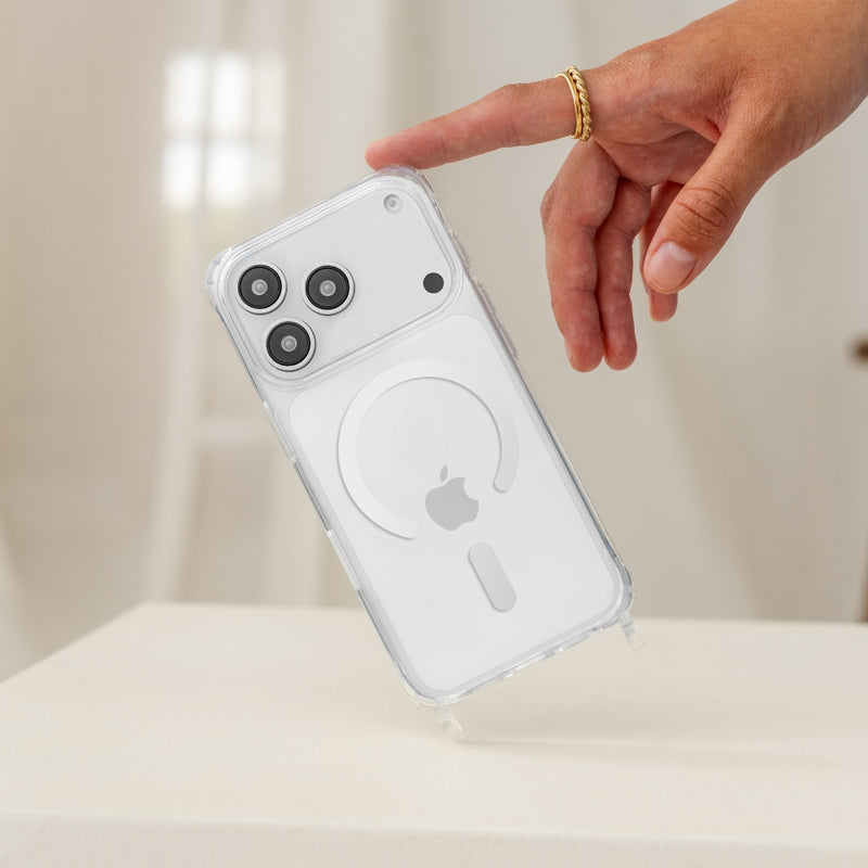 A hand is balancing a white iPhone 17 Pro in a transparent Clear Case , held at a slight angle with the index finger. At the bottom edge of the Case , the two transparent mounting loops for a Crossbody Case are clearly visible. Light, neutral background.
