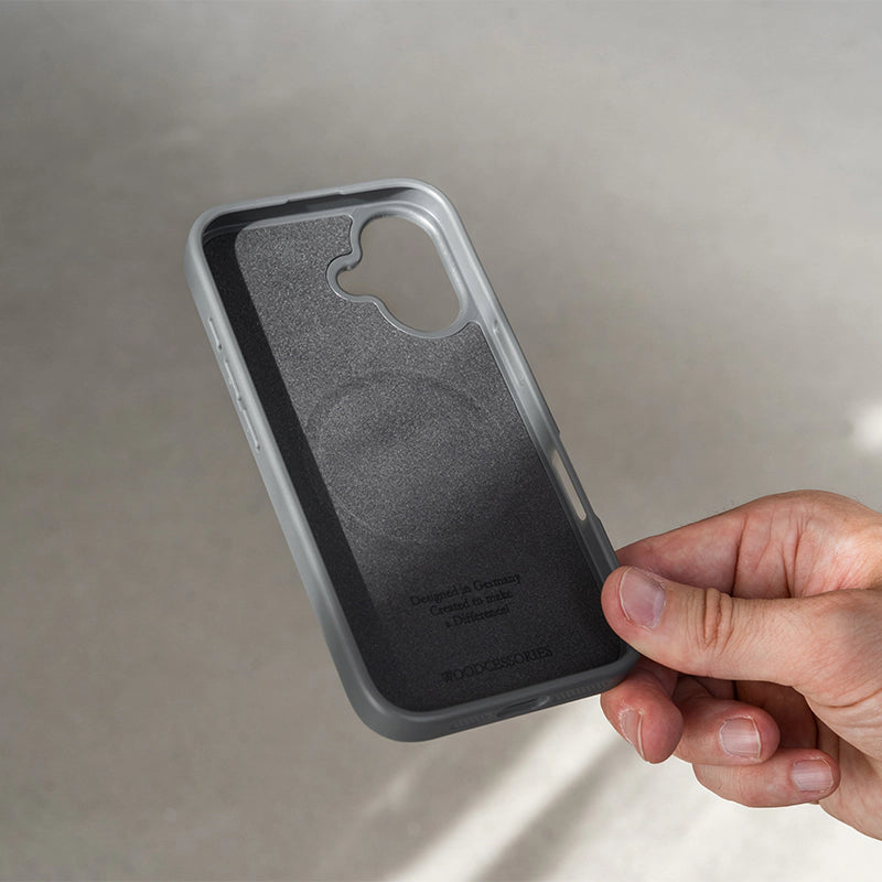 Hand zeigt die weich gepolsterte Innenseite des schwarzen iPhone 16 Bumper Case in Walnuss mit integriertem MagSafe-Ring und Woodcessories-Prägung.