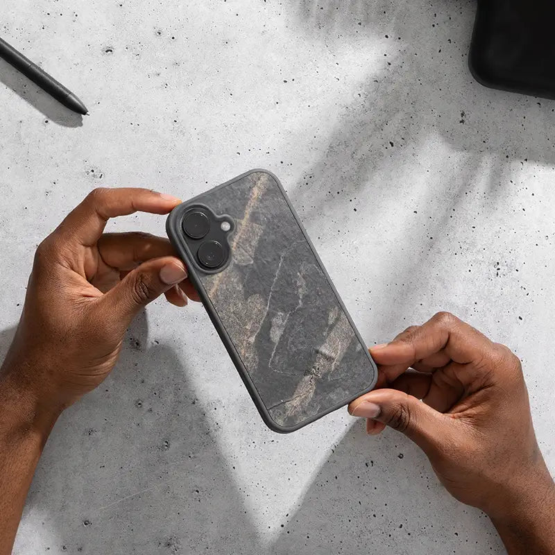 Person hält ein iPhone 16 im Bumper Case mit Stein in Nahaufnahme vor hellem Hintergrund in den Händen.
