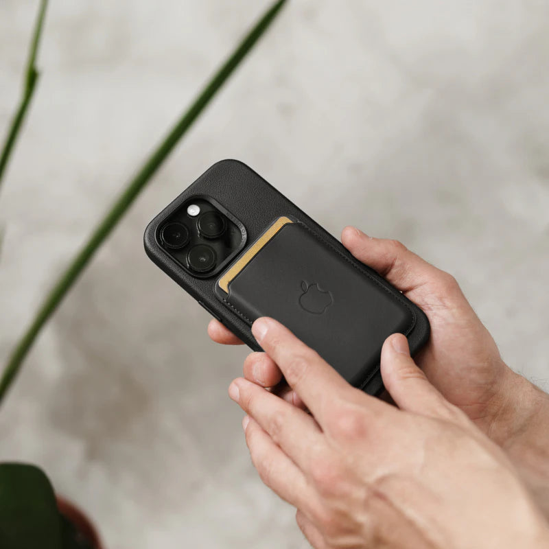Person hält ein iPhone 16 Pro Max im schwarzen Leder-Case mit einem schwarzen MagSafe Wallet auf der Rückseite.