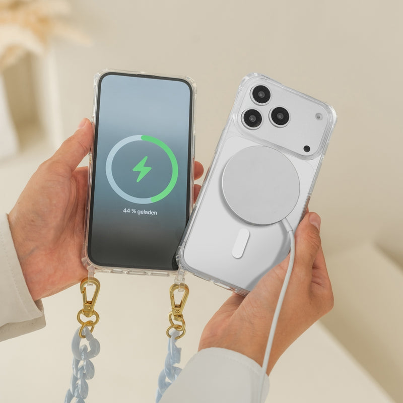 A person is holding two white iPhone 17 Pro models in clear cases: The device on the left shows the display with a green MagSafe charging animation and has a chunky " Crossbody Case " attached. The device on the right shows the back with a MagSafe charger connected.