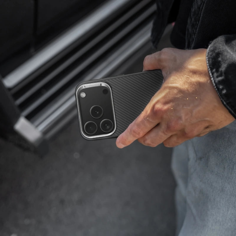 A person is holding a black iPhone 18 Pro with a Woodcessories Carbon Case case in front of a gray background.